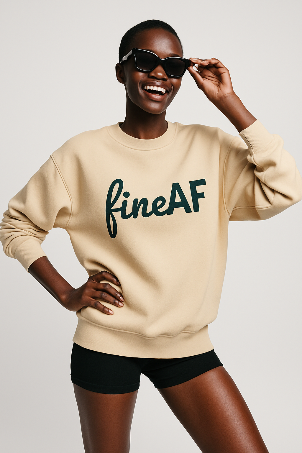 Person wearing a beige FineAF sweatshirt with a logo on it 'fineAF' text and black shorts, holding sunglasses.