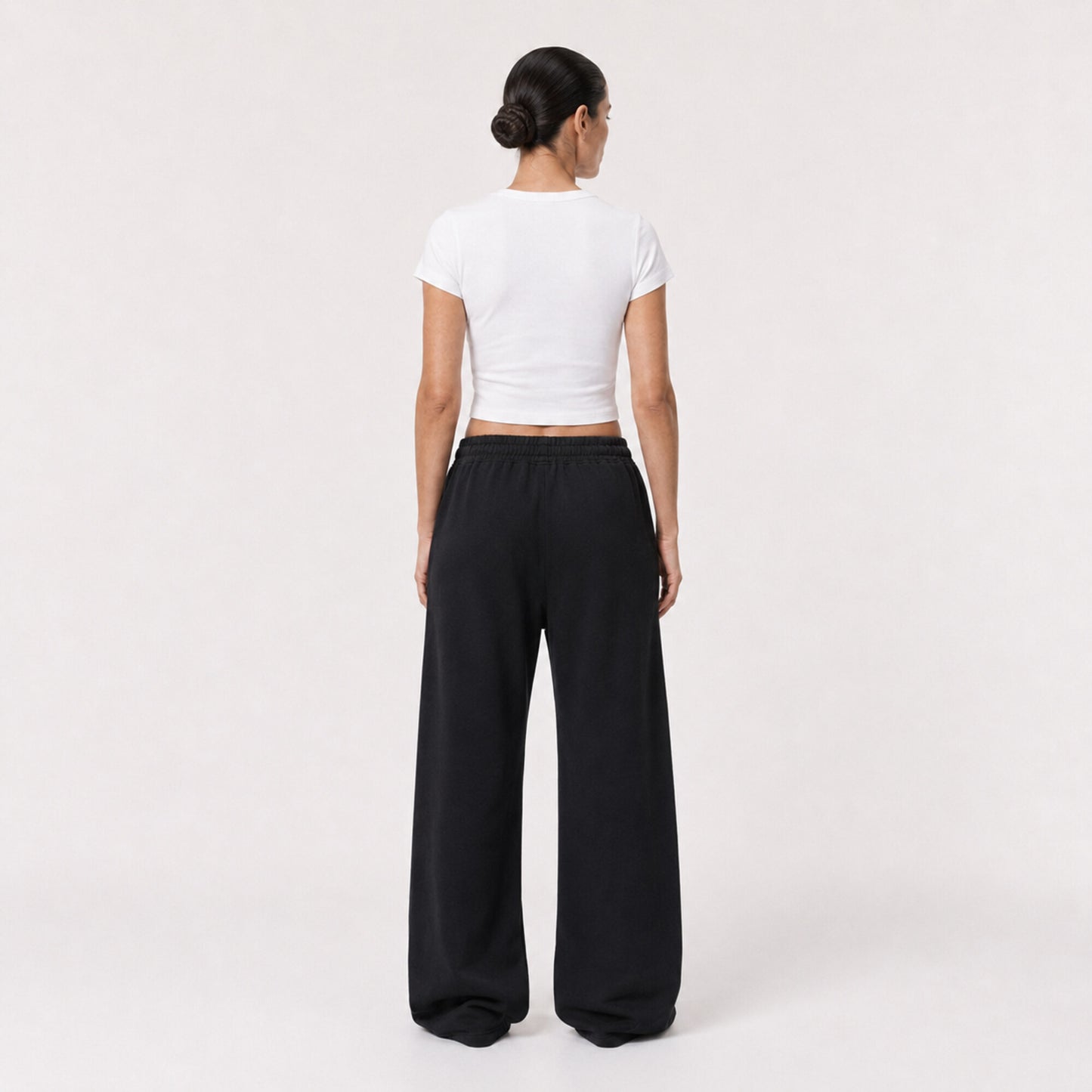 Back view of the white FineAF Cropped Tee worn with black wide-leg pants