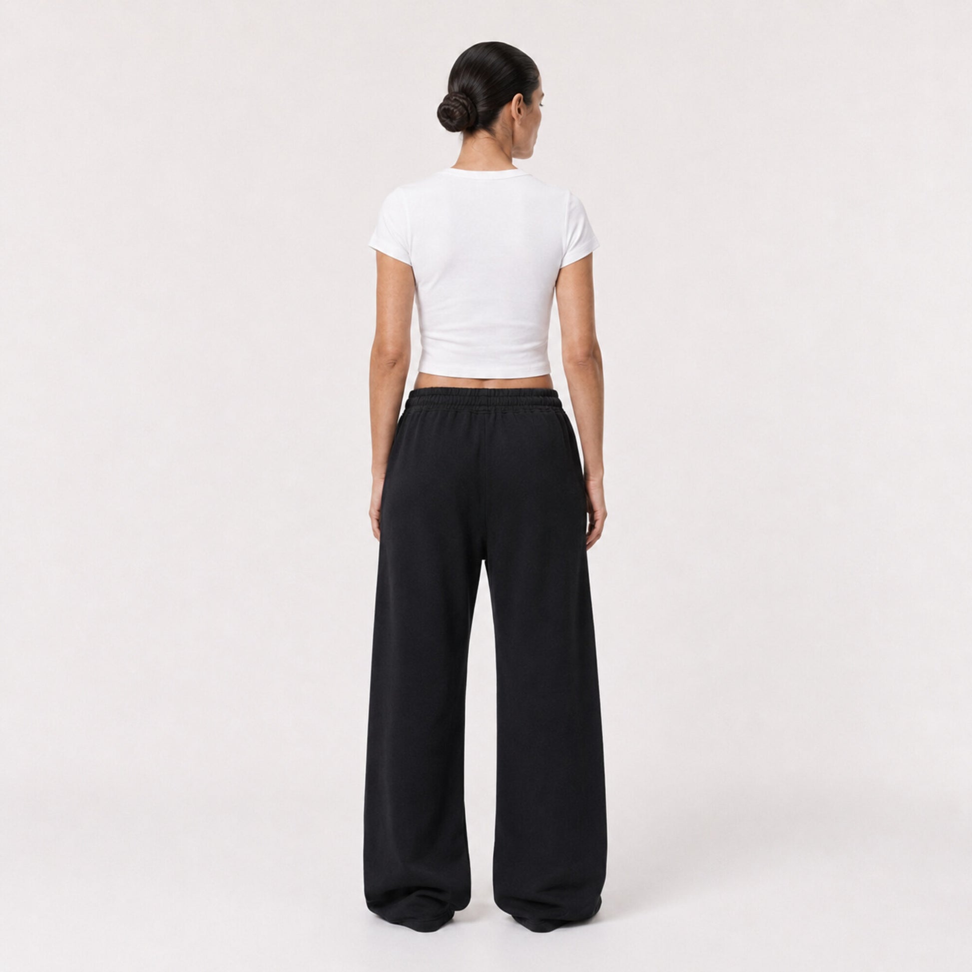 Back view of the white FineAF Cropped Tee worn with black wide-leg pants