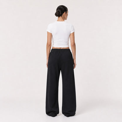 Back view of the white FineAF Cropped Tee worn with black wide-leg pants