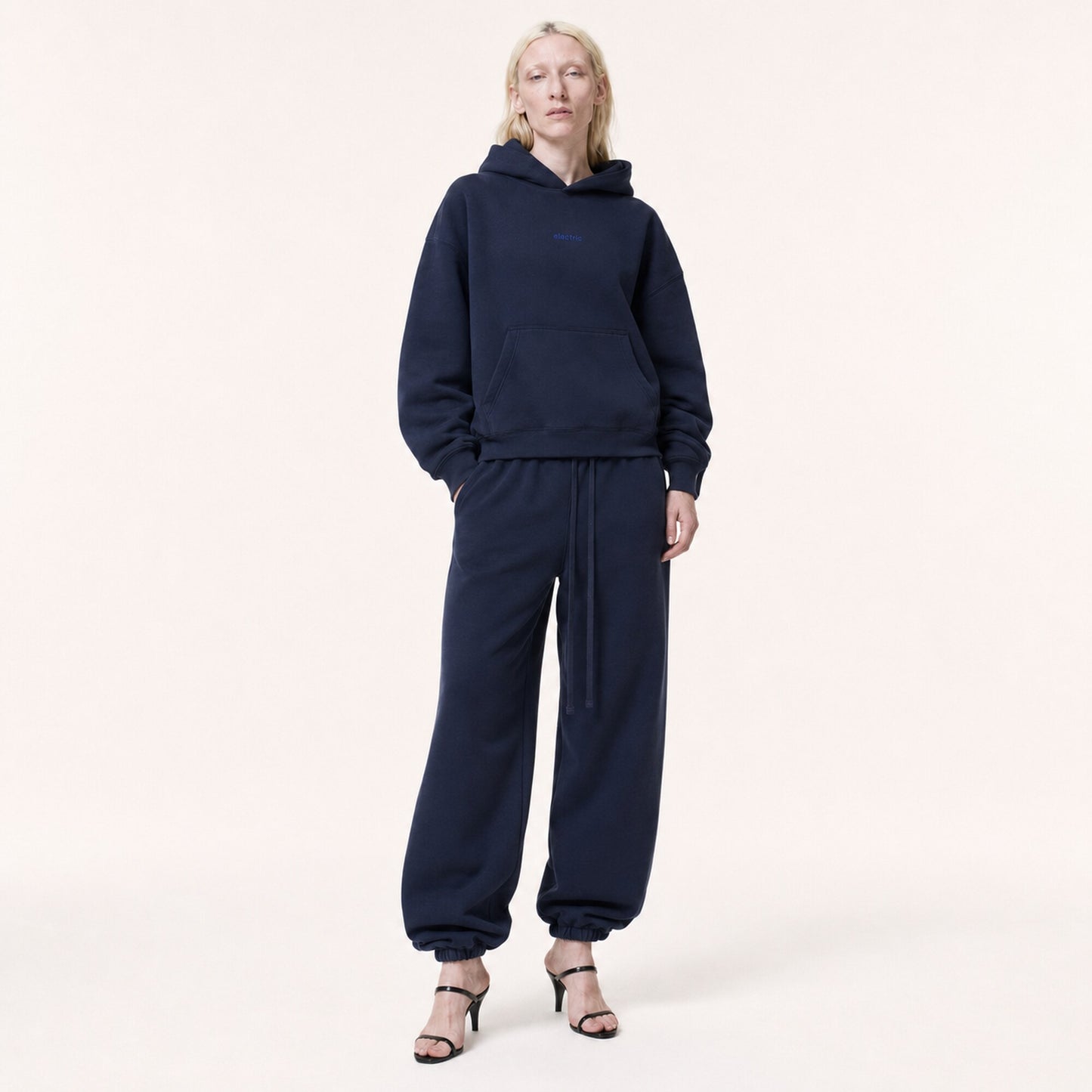 Woman wearing FineAF Electric deep navy oversized tapered pants with a matching hoodie and black heeled sandals, front view.