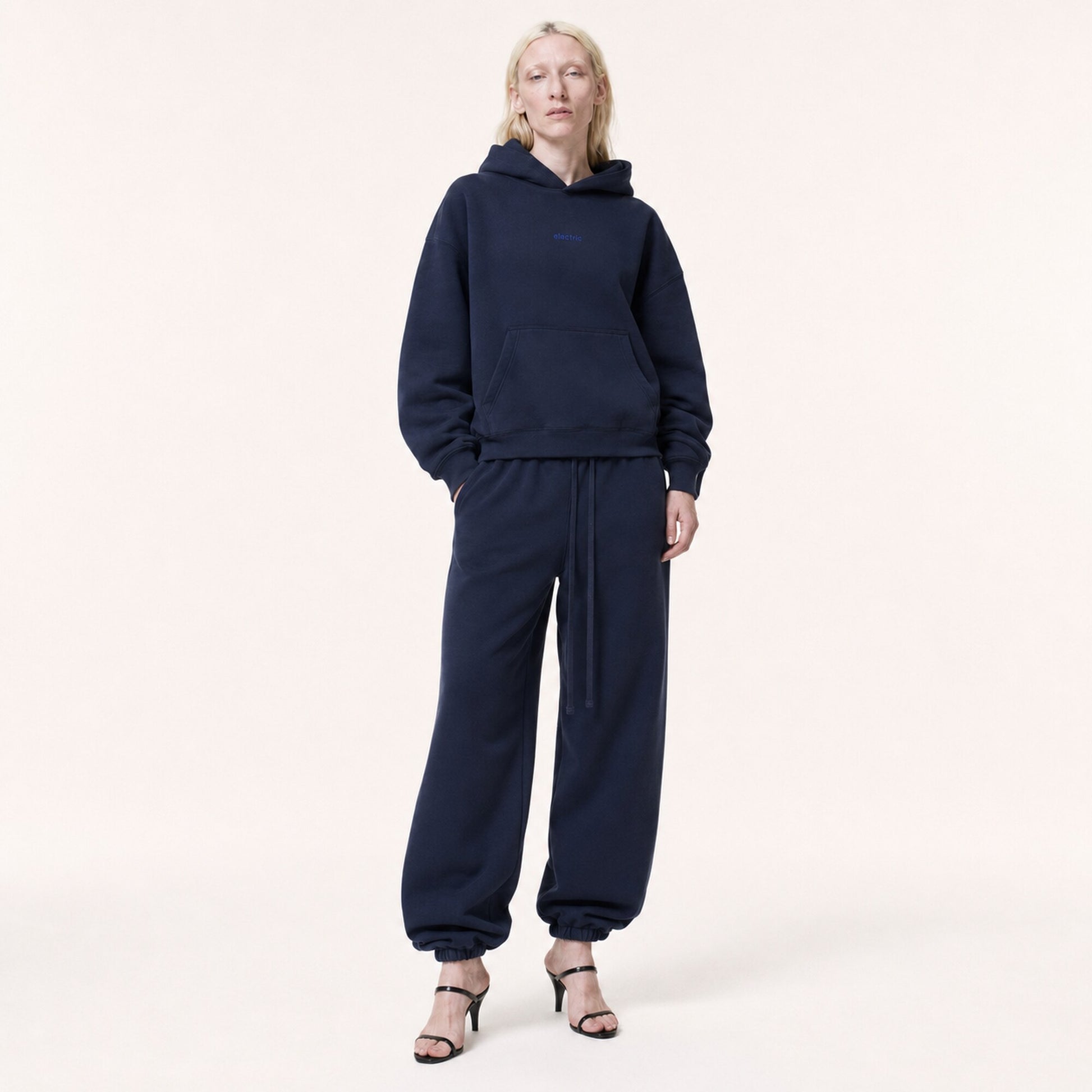 Woman wearing FineAF Electric deep navy oversized tapered pants with a matching hoodie and black heeled sandals, front view.