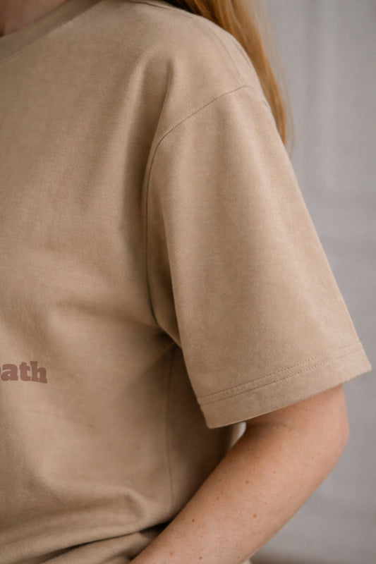 Beige FineAF crewneck T-shirt sleeve and side seam detail close-up showing fabric drape.