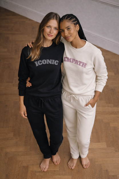 Two women wearing black and white sweatsuits with 'Iconic' and 'Empath' text on a wooden floor.