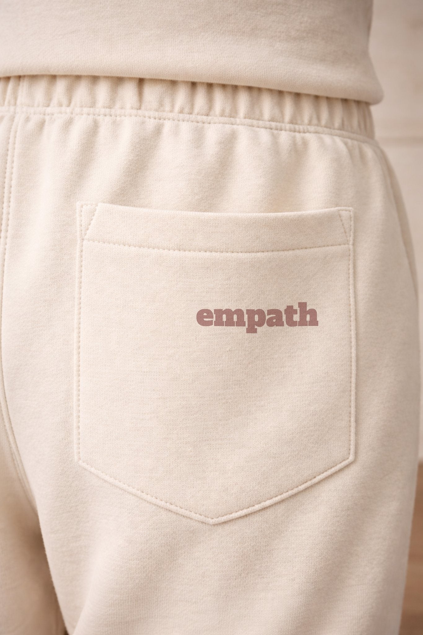 Beige sweatpants with 'empath' text on the pocket against a beige background
