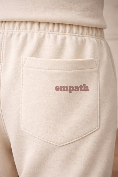 Beige sweatpants with 'empath' text on the pocket against a beige background