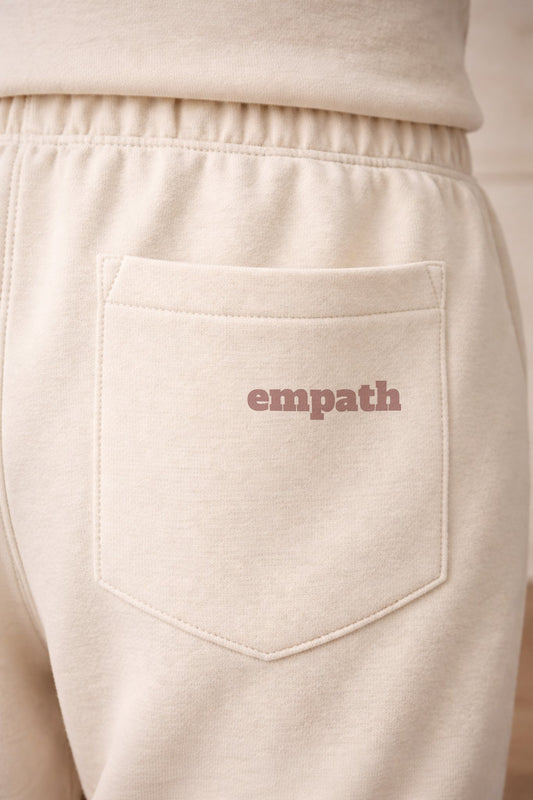 Beige sweatpants with 'empath' text on the pocket against a beige background