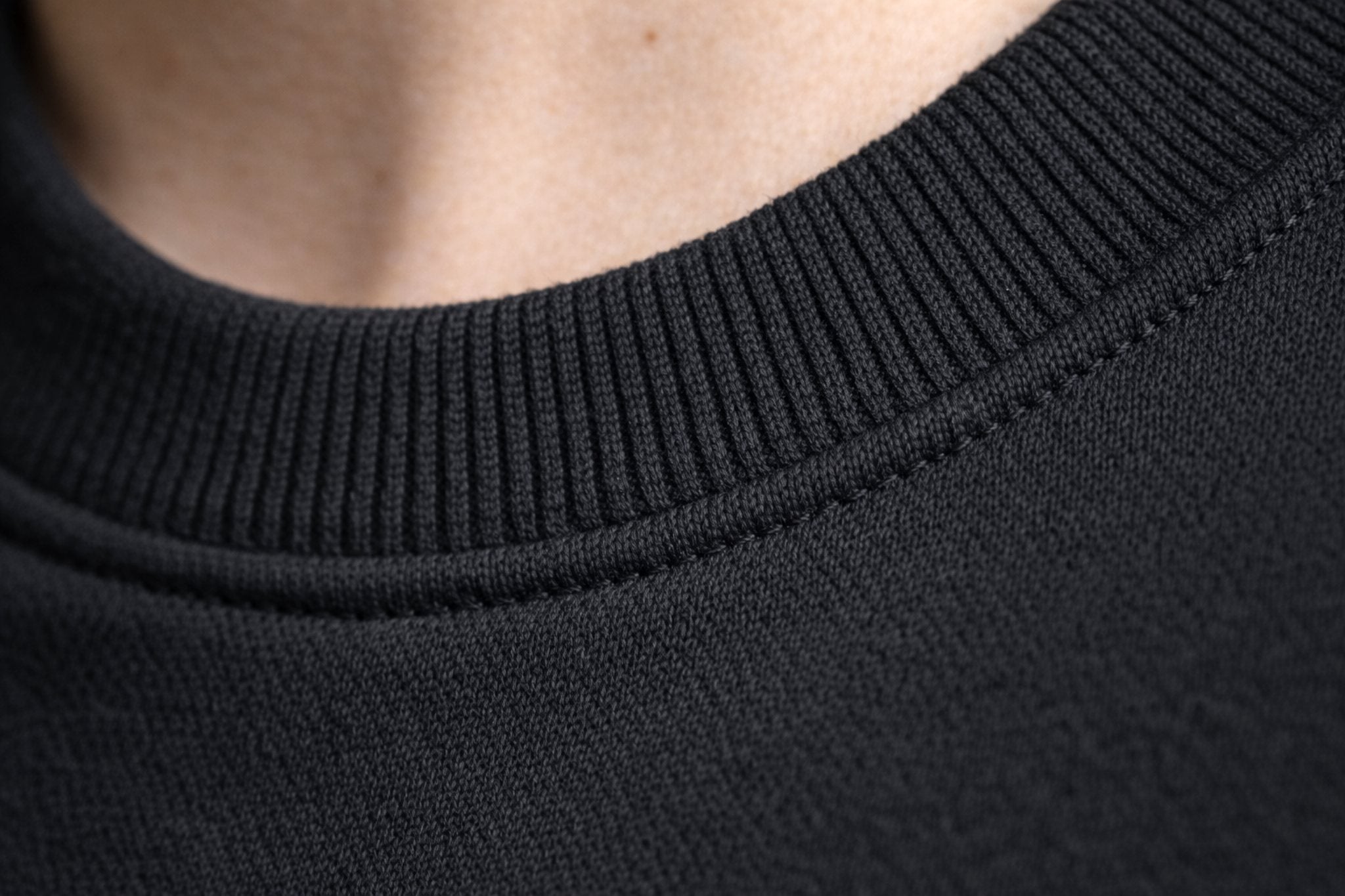 Close-up of black crewneck sweatshirt ribbed collar and stitched neckline seam.
