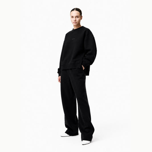 Model wearing the FineAF Iconic black oversized side-slit crewneck sweatshirt with matching black trousers in a bright white studio.