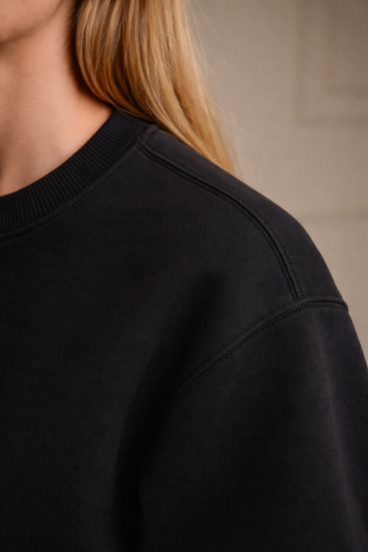 Black FineAF crewneck sweatshirt shoulder and neckline seam detail, close-up side view.