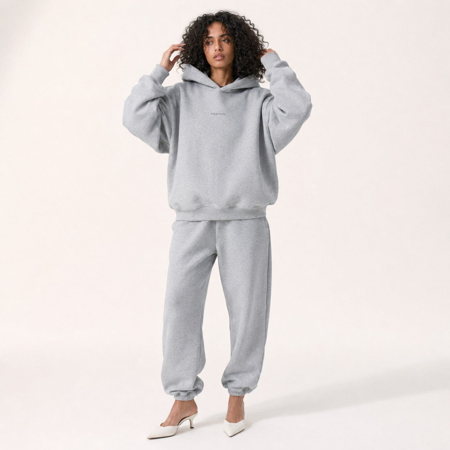 Model adjusting her hair in the FineAF Magnetic heather grey hoodie, showing its structured sleeves and hood