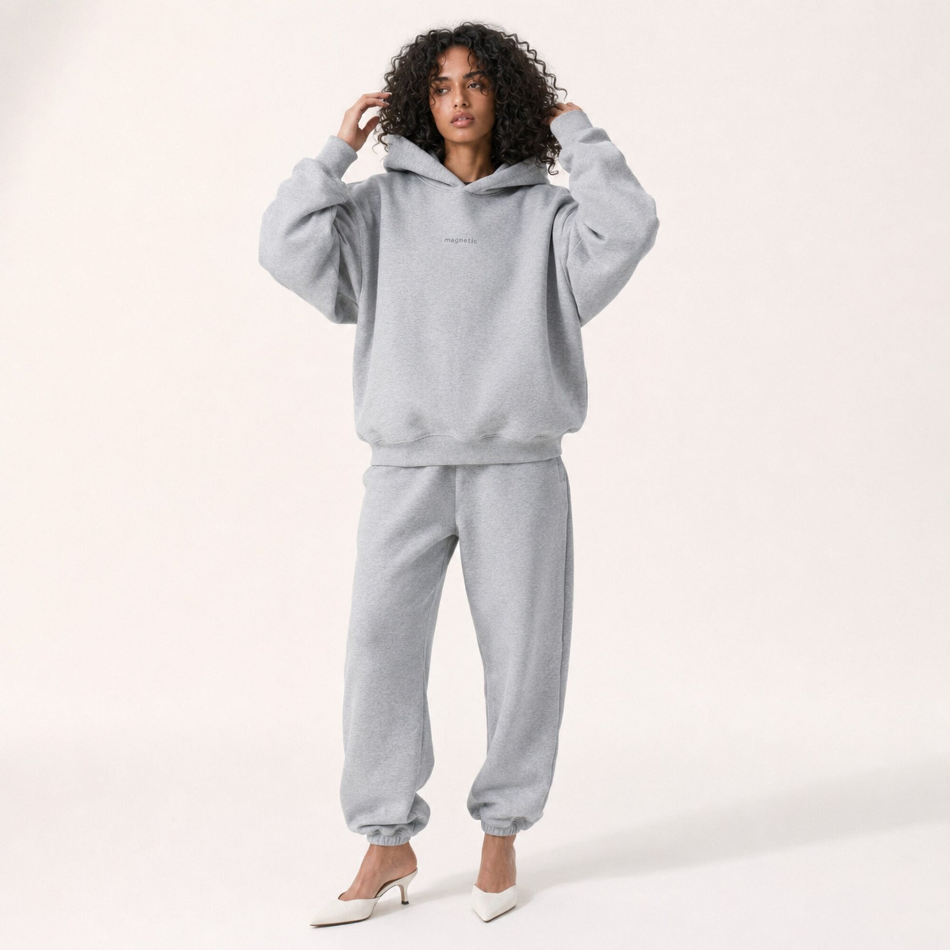 Model adjusting her hair in the FineAF Magnetic heather grey hoodie, showing its structured sleeves and hood