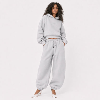 Woman wearing oversized light grey FineAF Magnetic pants and matching hoodie with white pointed heels, front view