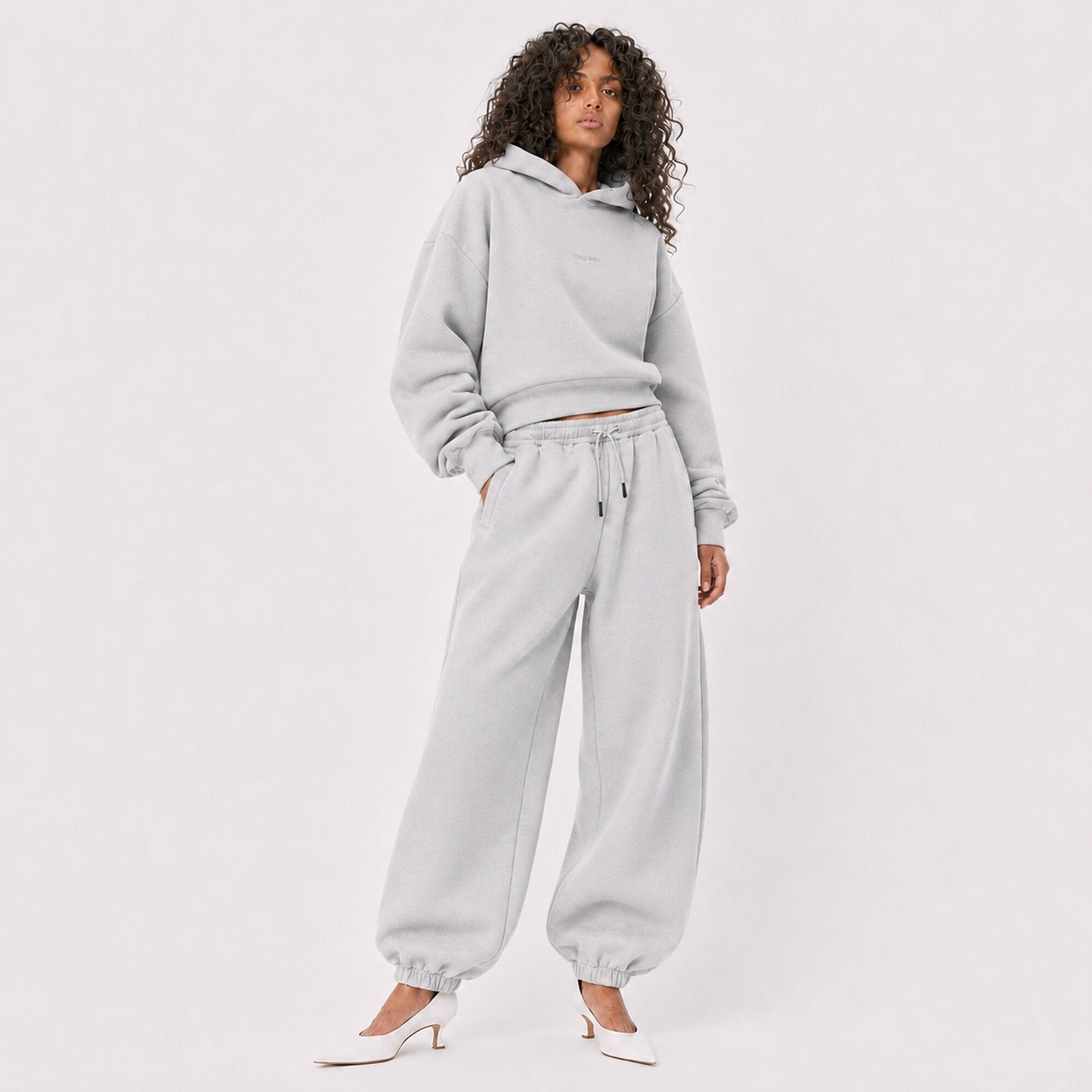 Woman modelling oversized light grey FineAF Magnetic pants and matching hoodie in a three-quarter studio view