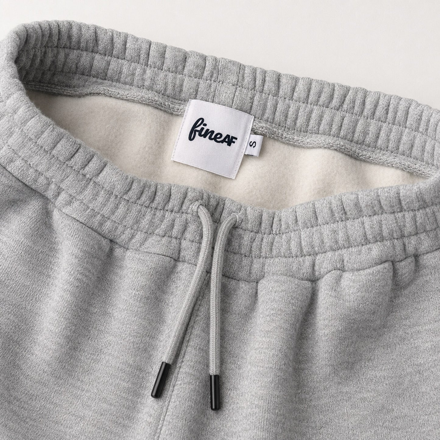 Close-up of FineAF Magnetic pants waistband, black-tipped drawcord, brushed interior and FineAF size S label