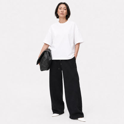 Woman wearing the white FineAF Boxy Tee with black wide-leg pants in a bright studio