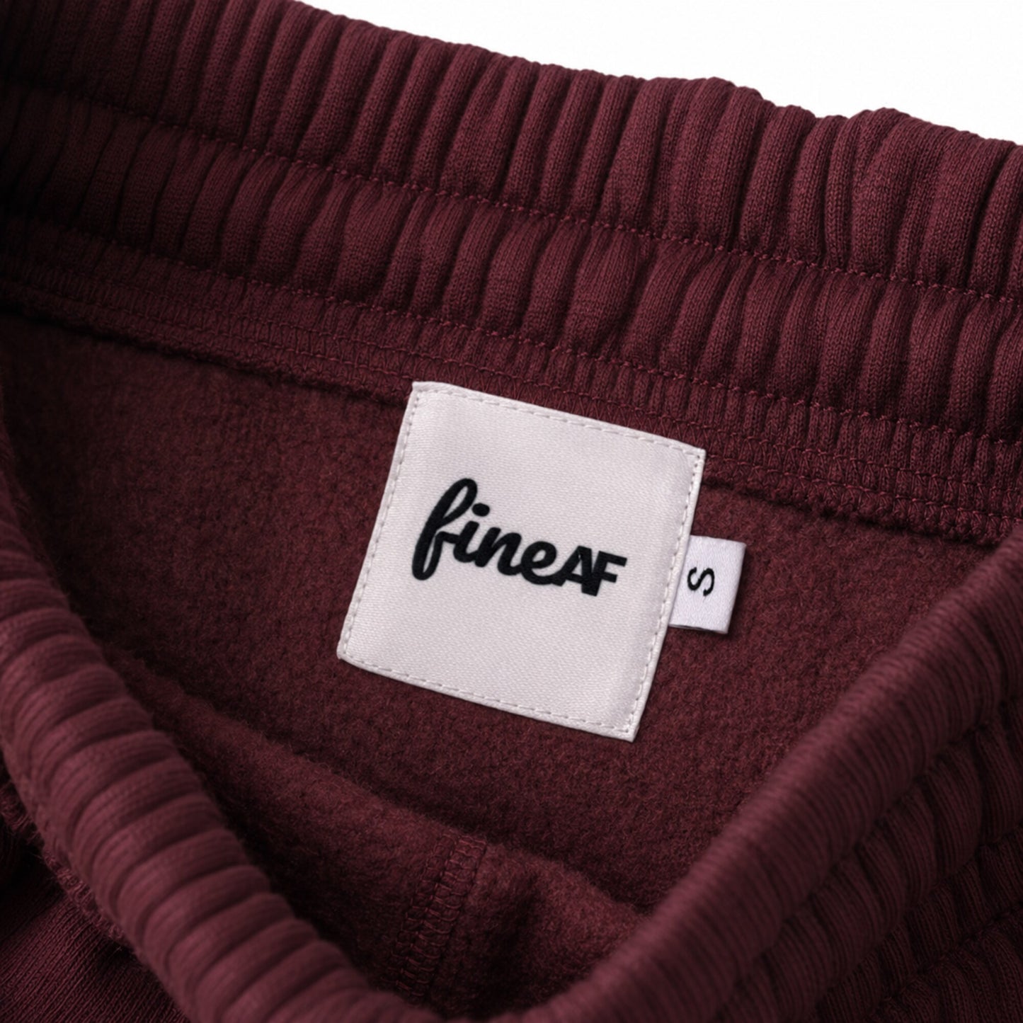 Inside waistband of FineAF Visionary wine pants with white FineAF woven label and S size tab.