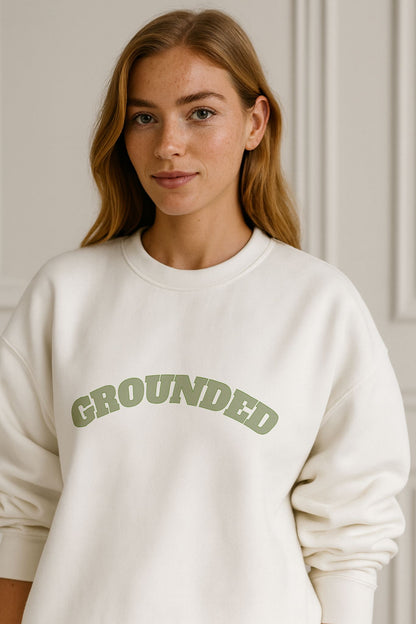 Woman in white FineAF GROUNDED sweatshirt, organic cotton fleece, soft green lettering, luxury casual style.
